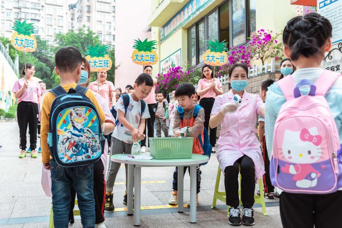 School children wearing masks get their temperatures checked and hands sanitized by teachers in a school