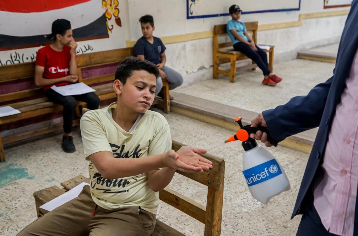 A boy sits at his desk in school and gets his hands sanitized